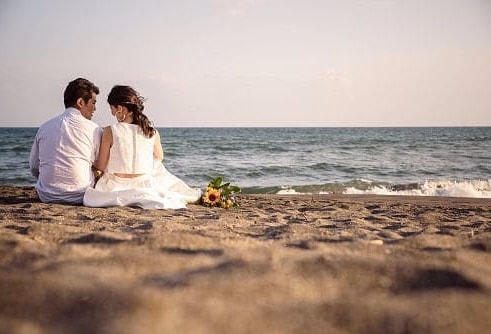 砂浜に座ってる新郎新婦の後ろ姿