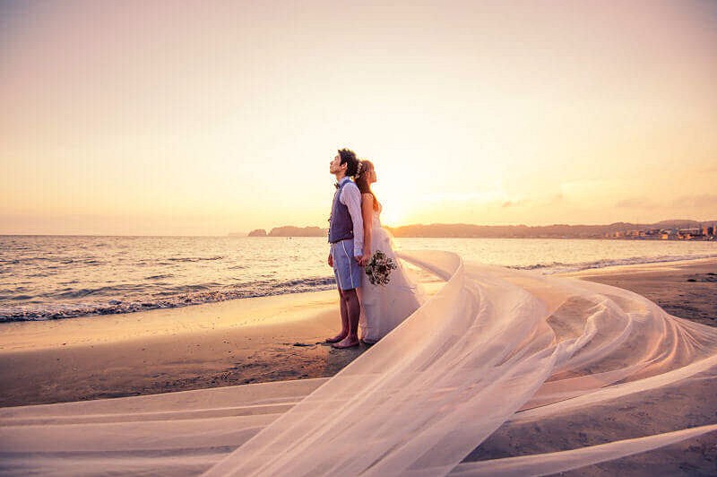 綺麗な夕日と風でなびく新婦のウェディングベール