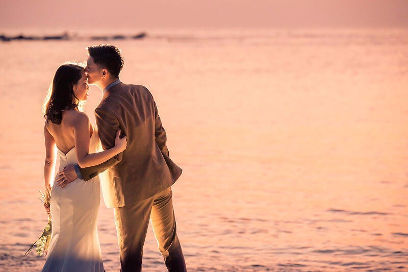 ロマンチックな夕焼けを背景にキスする新郎