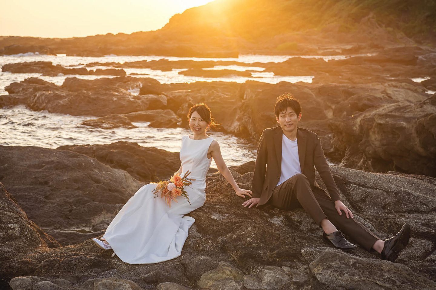 夕日に照らされた岩場に座るふたり