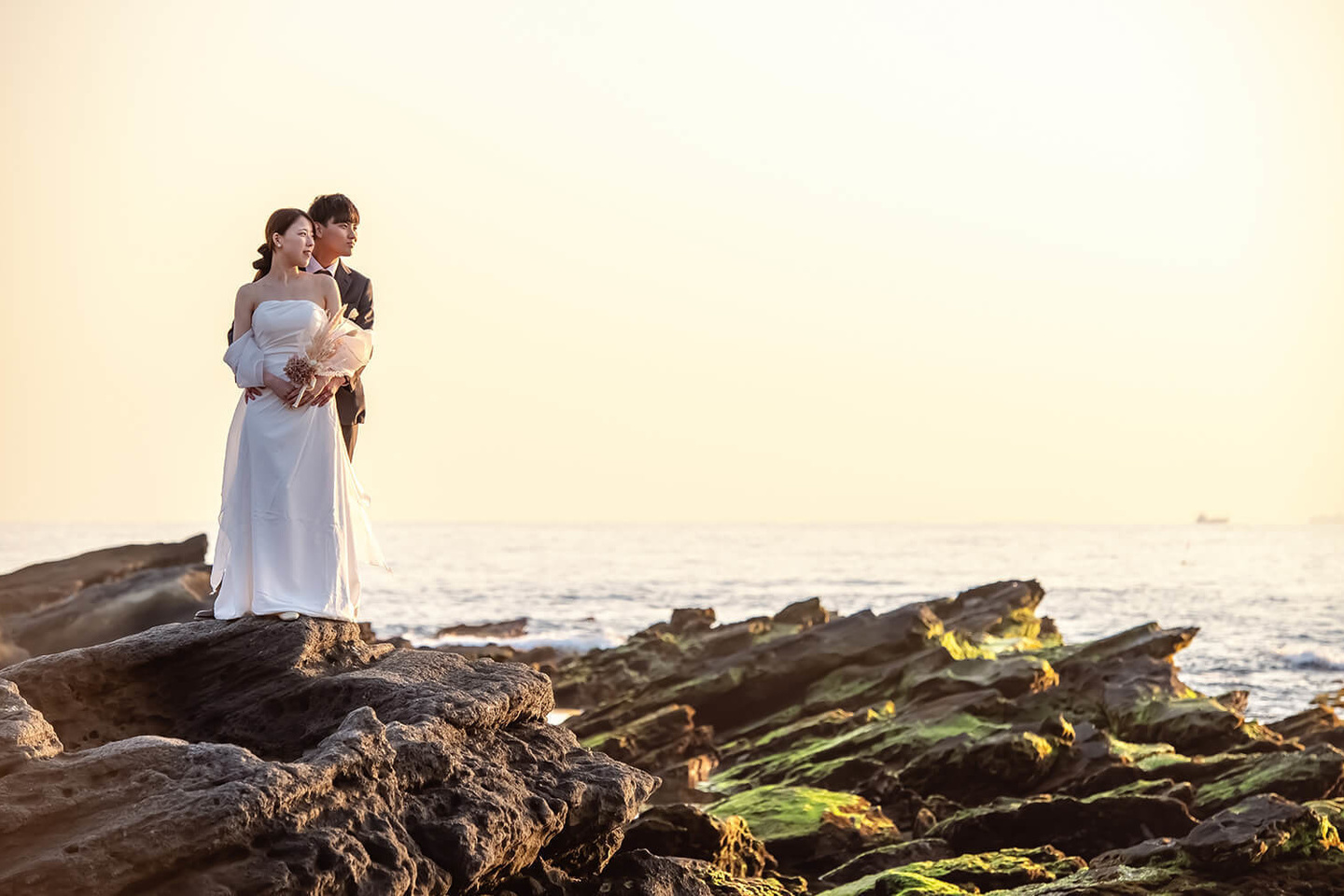 岩場に立って太陽を見る新郎新婦